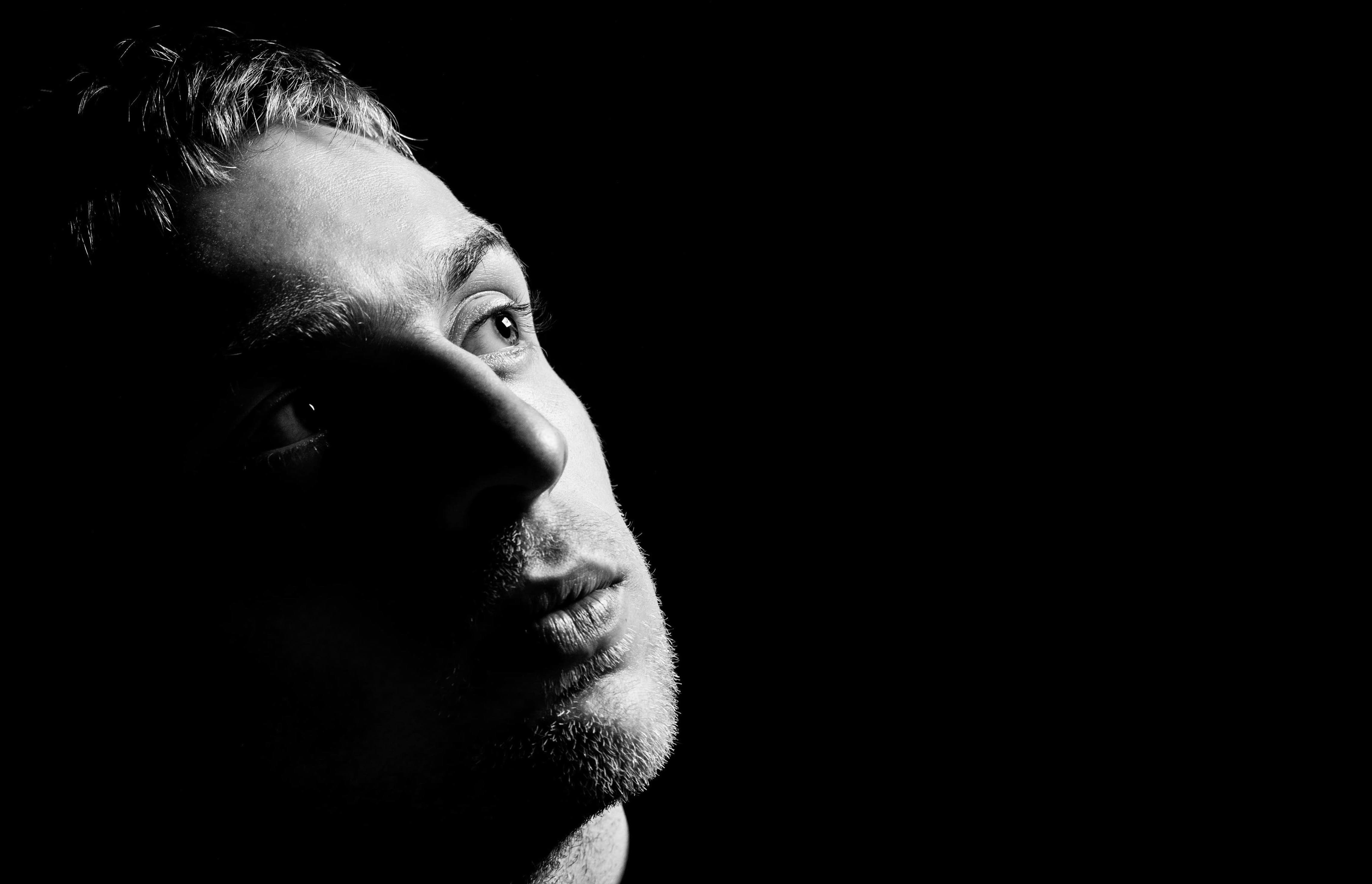 Man looking up with a dark background, black and white image, studio light illuminating his face.